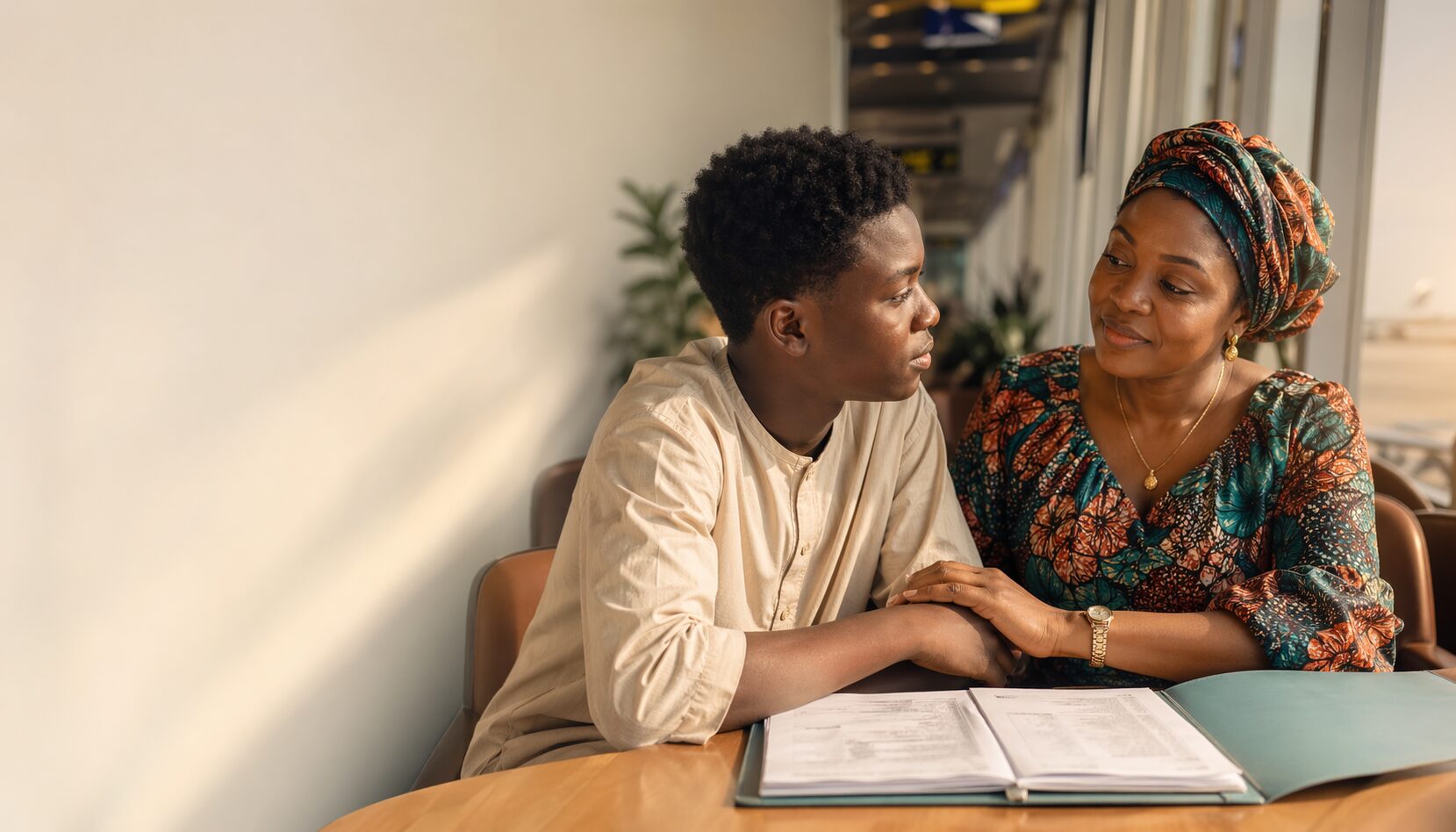 Nigerian mother and teenage son reviewing medical documents together in a warm airport lounge before traveling to India for treatment